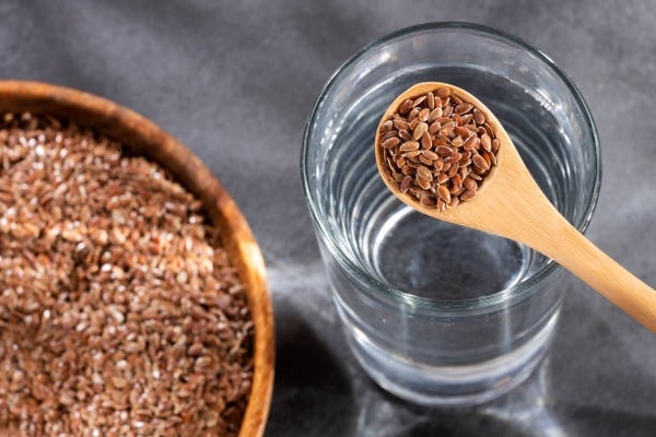 Linum usitatissimum Spoon with organic flaxseeds and glass of filtered water
